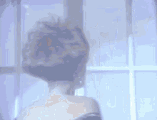 a woman is dancing in front of a window in a room with her hair blowing in the wind .