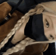 a woman with blonde hair is wearing a black mask and braids .