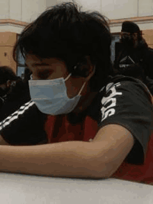 a young boy wearing a face mask is sitting at a table in a classroom .