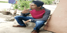 a young man wearing a baseball cap and a red shirt is sitting on the sidewalk