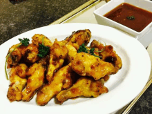 a white plate topped with chicken wings next to a small bowl of dipping sauce