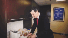 a man in a suit and tie is preparing food in a kitchen with a huff post canada poster in the background