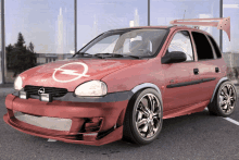 a red opel car with chrome wheels is parked in a parking lot