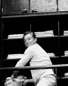 a black and white photo of a man sitting on a railing in front of a shelf full of clothes .