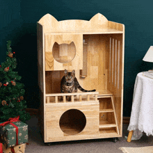 a cat is sitting in a wooden house with a christmas tree in the background