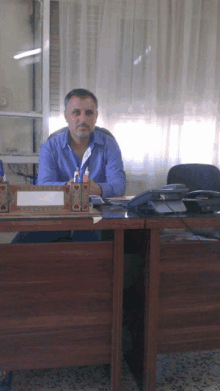 a man in a blue shirt sits at a desk with a name holder that says ' abdullah ' on it