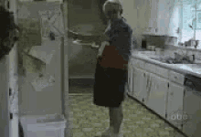 an elderly woman is standing in a kitchen holding a spoon .