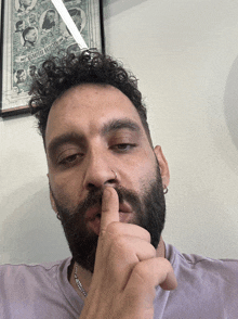 a man with a beard holds his finger to his nose in front of a framed picture that says barbers