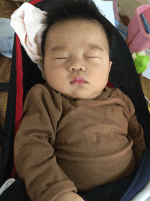 a baby in a brown shirt sleeping in a bouncer