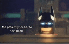 a batman helmet is sitting on a table and says me patiently for her to text back