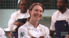 a woman in a chef 's uniform is smiling while standing in front of a group of men in aprons .