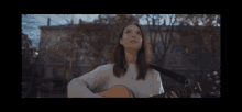 a woman in a white sweater is playing an acoustic guitar