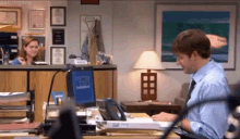 a man in a blue shirt and tie is sitting at a desk in front of a computer in an office .