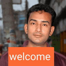 a man holds a sign that says welcome in front of his face