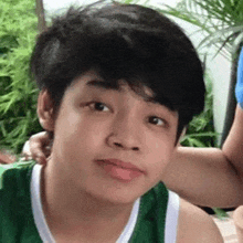 a young boy wearing a green and white tank top is looking at the camera and making a funny face .