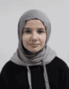 a woman wearing a hijab and a black hoodie is standing in front of a white background .