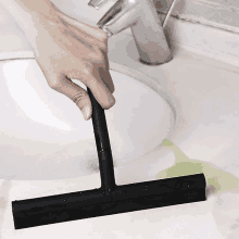 a person is using a black rubber squeegee to clean a sink