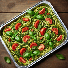 a pan of spaghetti with pesto and tomatoes on a wooden table