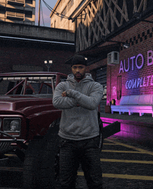 a man in a grey hoodie stands in front of an auto body complete sign