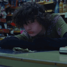 a young man in a green shirt with a purple star on it sits at a counter in a store