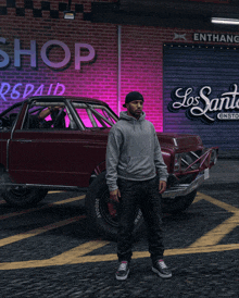 a man in a grey hoodie stands in front of a los santos sign