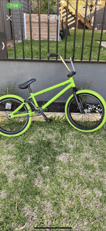 a green bmx bike is parked in front of a fence