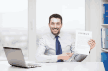 a man is sitting at a desk holding up a contract