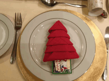 a plate with a napkin folded in the shape of a christmas tree and a secret santa card