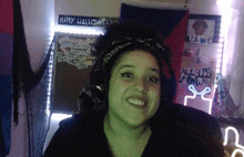 a woman wearing headphones and a headband is smiling in front of a sign that says `` happy halloween '' .