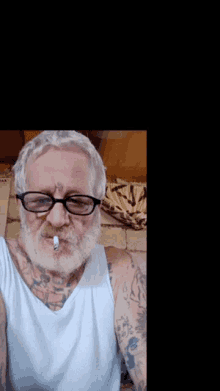 a man wearing glasses and a white tank top has a cigarette in his mouth