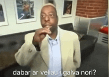 a man in a suit is eating a piece of food with the words dabar ar veliau i galva nori behind him