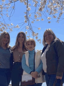 a group of women standing under a tree with flowers