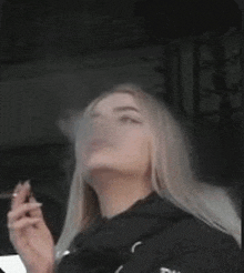 a woman is smoking a cigarette in a car while wearing a black jacket .