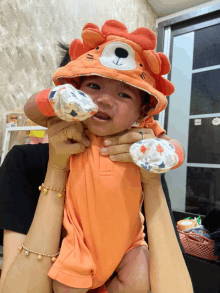 a baby wearing an orange outfit with a lion hat