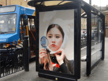 a bus stop has a poster of a girl looking at herself in a mirror