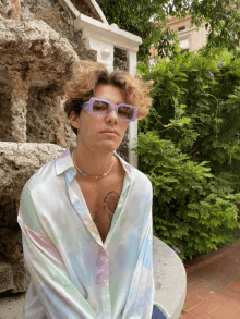 a young man wearing sunglasses and a tie dye shirt has a tattoo on his chest