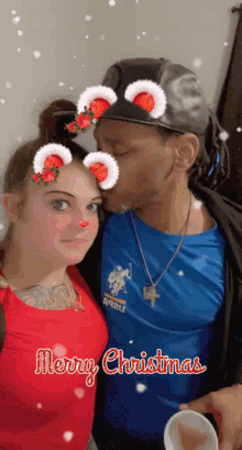 a man kisses a woman on the cheek with a merry christmas greeting behind them