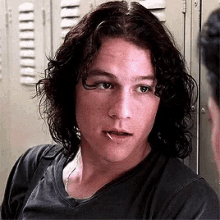 a young man with long curly hair and a piercing in his lip is standing in front of lockers .