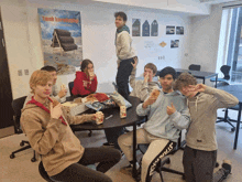 a group of young people sitting around a table with a poster on the wall that says " tenk bæredygtigt "