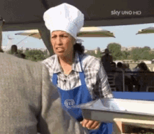 a woman in a chef 's hat and apron is holding a tray in front of a sign that says sky uno hd