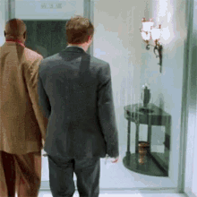 a man in a suit walks with another man in a tan jacket