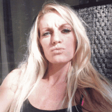 a woman with blonde hair and a black tank top looks at the camera