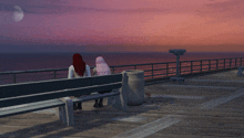 two women sit on a bench looking at the ocean