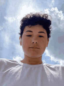 a young boy with curly hair is taking a selfie in front of a blue sky .