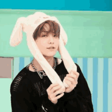 a young man wearing a bunny hat with moving ears is standing in front of a striped wall .