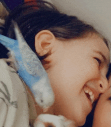 a little girl is holding a blue and white parakeet in her arms and smiling .