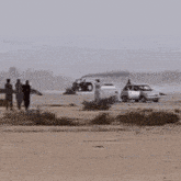 a group of people are walking on a sandy beach with cars parked on the side of the road .