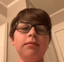 a young boy wearing glasses is taking a selfie in a bathroom .