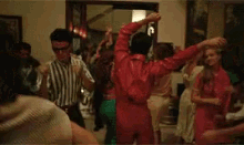 a man in a red jacket is dancing in a room with other people