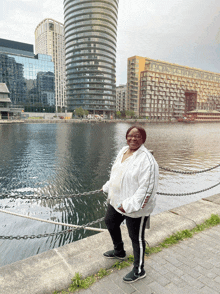 a woman wearing a white jacket with the word nike on it stands in front of a body of water